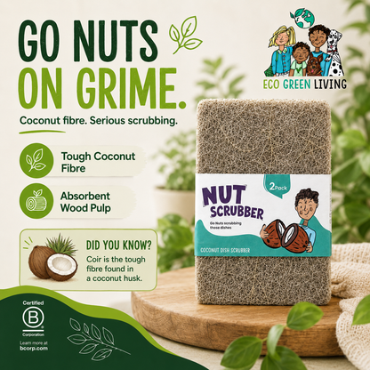 A packaged coconut fiber scrubber standing on a wooden board with decorative leaves and a soft green background. The product has a white label reading 'NUT SCRUBBER' and 'COCONUT DISH SCRUBBER,' with '2 pcs' at the top right.